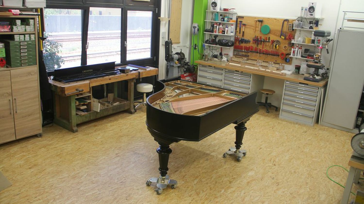 L'atelier de Bühler Pianos à Yverdon-les-Bains, un piano à queue au centre et l'établi le long de la fenêtre