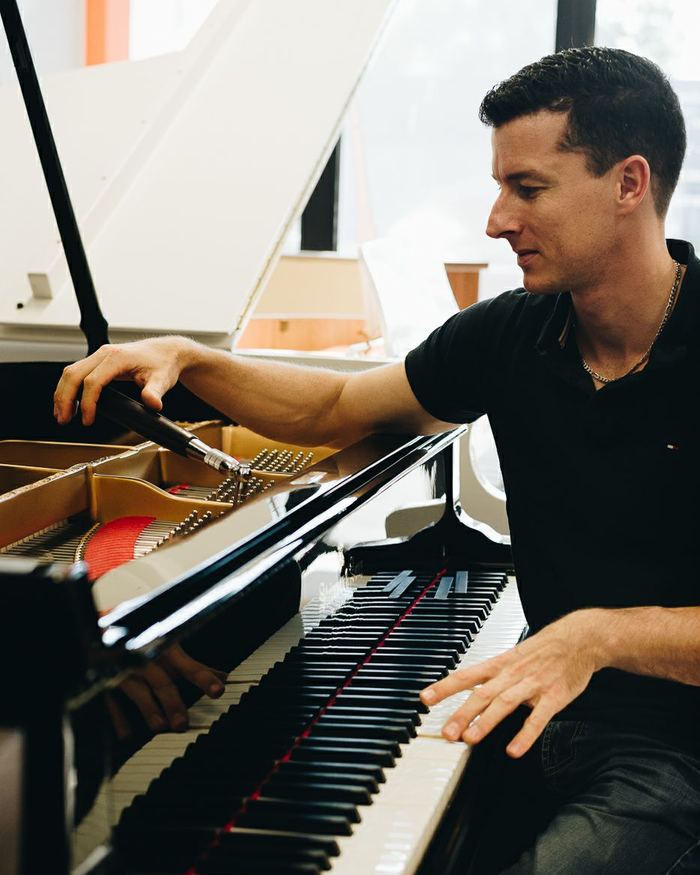 Frank Bühler au clavier d'un piano à queue dans son atelier